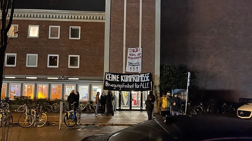 Menschen stehen vor einer Kirchengemeinde in Bremen, über deren Tür Banner gehisst sind. Sie protestieren gegen eine Abschiebung aus dem Kirchenasyl.