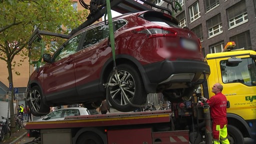 Ein dunkelrotes Auto wird vom Abschleppdienst mitgenommen, weil es falsch parkt. 