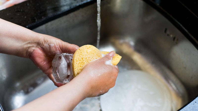 Zwei Hände spülen Geschirr in der Spüle.