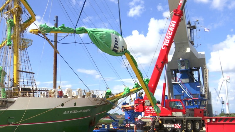 Eine Rahe der "Alexander von Humboldt II" wird von einem Kran in die Höhe gehoben.