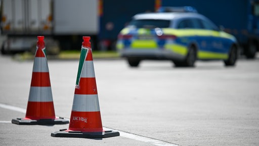 Pylonen stehen auf einer Straße, im Hintergrund ist ein Polizeiauto zu sehen.