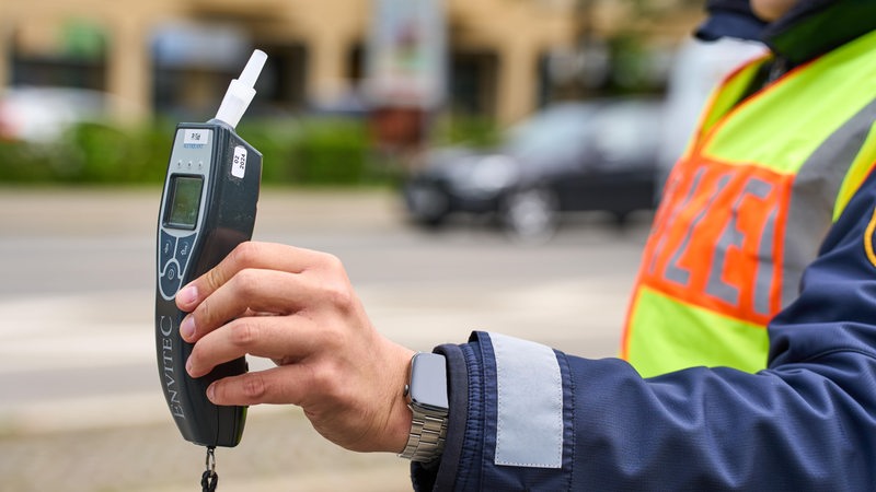 Ein Polizist hält ein Alkoholtestgerät in der Hand.