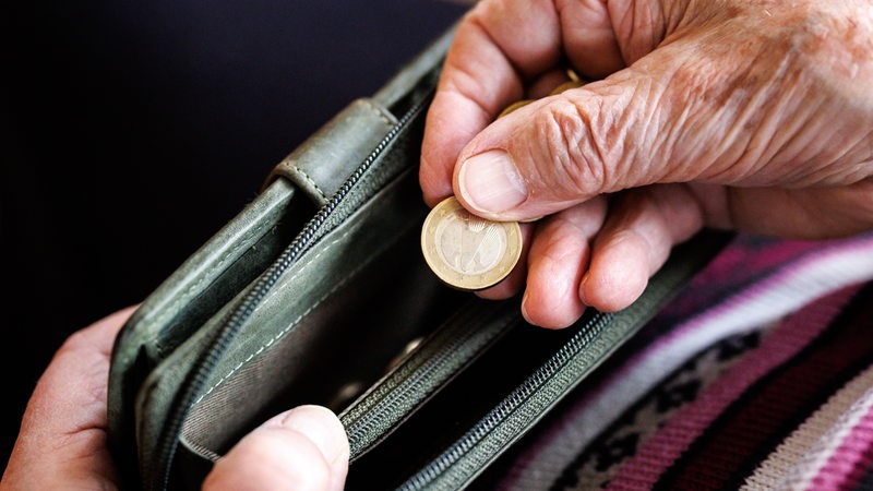 Die Hand einer älteren Frau hält eine Geldtasche, aus der sie ein 1-Euro-Stück nimmt.