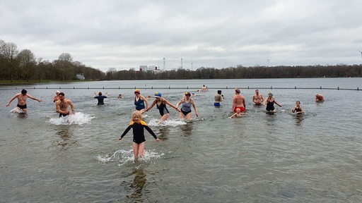 Menschen in Badeanzug und Badehose waten durch einen See