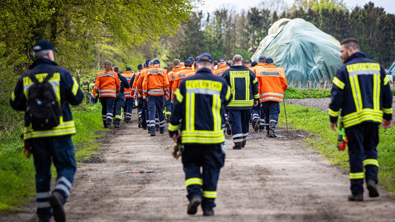 Einsatzkräfte der Feuerwehr gehen eine Straße im Landkreis Stade entlang.