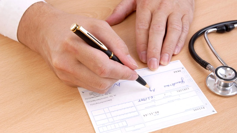 Eine Hand mit Kugelschreiber schreibt auf ein Papier.