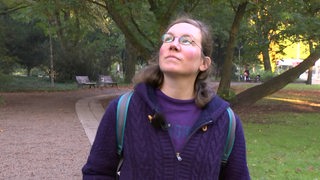 Eine junge Frau im Park blickt in den Himmel