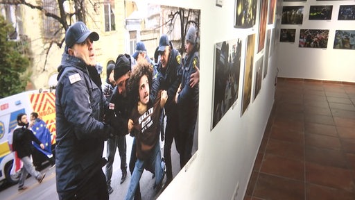 Ein Bild, auf dem ein georgischer Mann von Polizeibeamten festgehalten wird, hängt in einer Ausstellung.