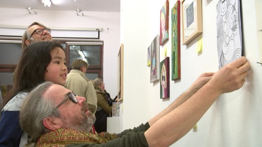 Ein Mann richtet ein Bild an der Wand. Es sieht aus wie eine Ausstellung.