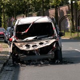 Ein ausgebranntes Auto steht am Straßenrand und ist mit Flatterband abgesperrt.