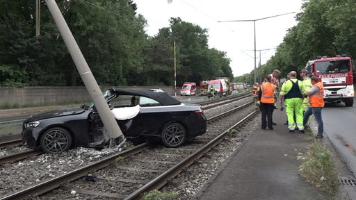 Ein Auto steht quer über den Schienen neben einem schiefen Oberleitungsmast.