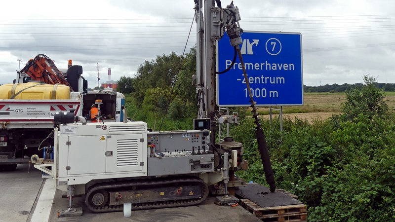 Ein Bohrgerät steht vor einem blauen Schild auf der Autobahn.