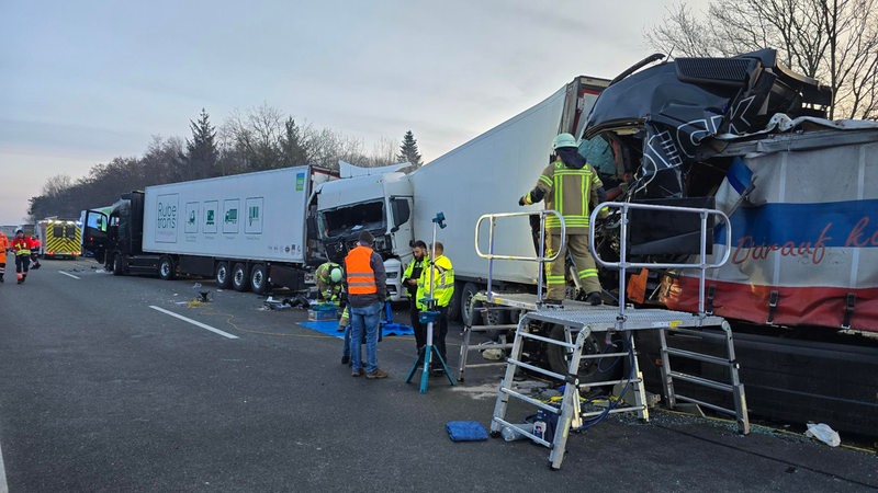 Polizisten und Feuerwehrleute sichern nach einem Unfall, bei dem mehrere Lkw aufeinander aufgefahren sind, die Unfallstelle ab.