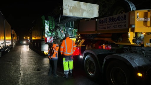 Fenja Bierwirth und eine weitere Person stehen im Dunkeln an einem großen Schwerlasttransporter