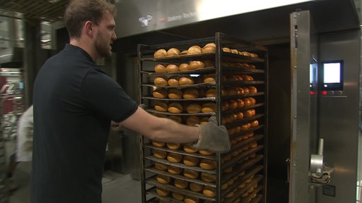 Ein Bäcker holt Brötchen aus einem Ofen.