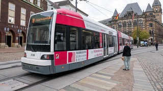 Eine Frau steht vor einer Straßenbahn in Bremen. 