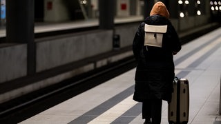 Eine Person steht am frühen Morgen während des Warnstreiks bei der Bahn mit Koffer auf einem Bahnsteig.