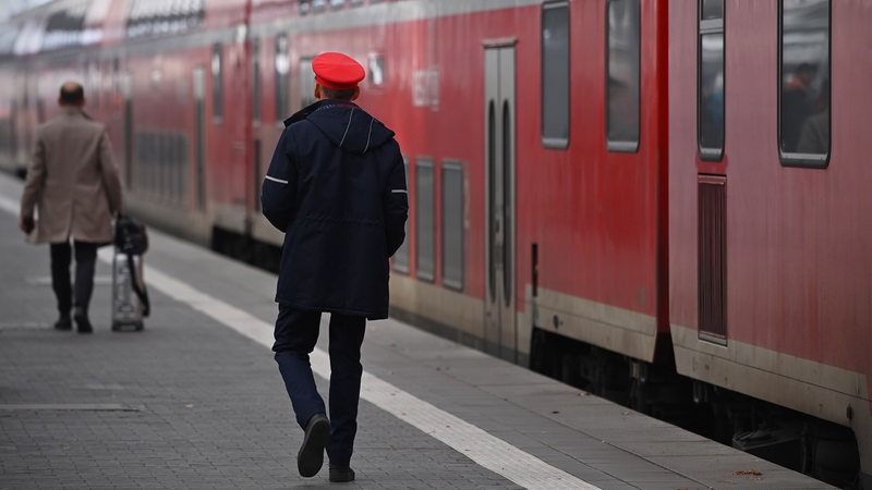 Bediensteter der Bahn geht auf dem Bahnsteig an einem Regionalzug entlang