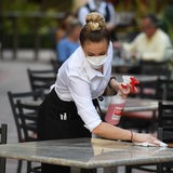  Eine Kellnerin mit Mund-Nasenschutz wischt Tische einer Außengastronomie sauber