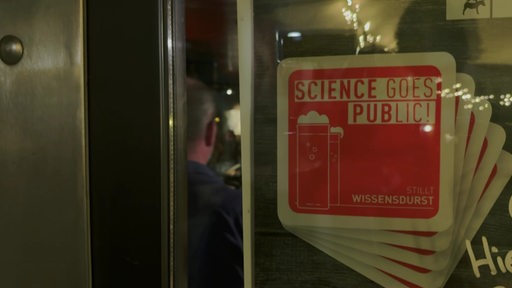 Eine Kneipe mit einem Schild davor. Auf dem Schild steh "Science goes public".