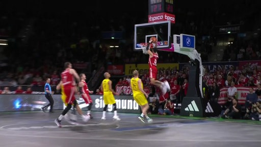 Ein Basketballspieler von Bayern München dunked den Ball in den Korb.