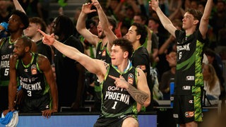 Basketballer Anzac Rissetto vom Klub South East Melbourne Phoenix streckt seinen rechten Arm aus und zeigt mit dem Zeigefinger in die Ferne,