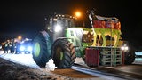 Ein Traktor transportiert das schwarz-rot-goldene Modell einer Kuh und steht gemeinsam mit anderen Traktoren auf einer Autobahn, die blockiert ist.