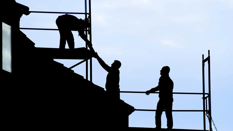 Dachdecker führen Arbeiten an einem Reihenhaus in Bremen durch. Sie sind nur als Silhouette vor dem hellen Himmel zu sehen.