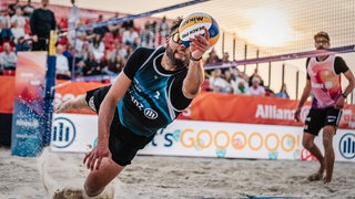 Ein Beachvolleyballspieler hechtet nach einem Ball.