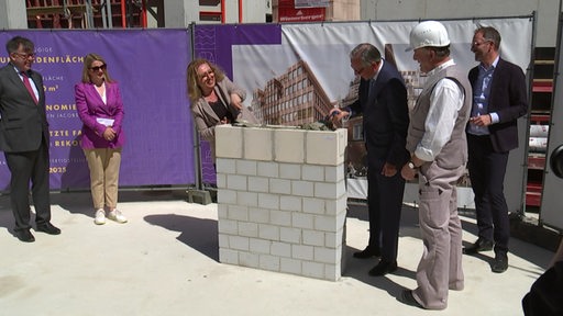 Die Bausenatorin und der Bauherr betonieren eine Steinmauer zu.