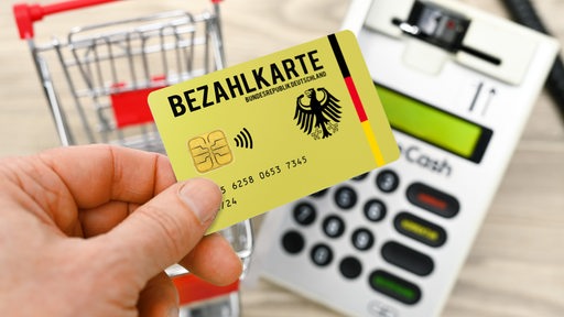 eine Hand mit Bezahlkarte vor einem Kartenlesegerät