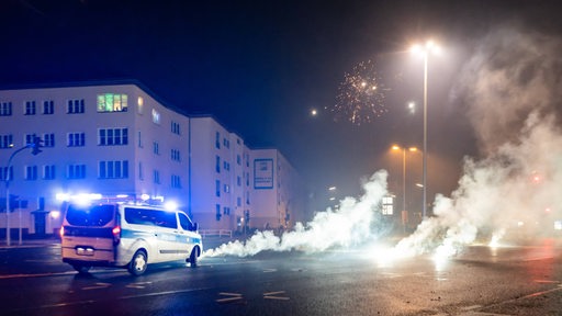 Ein Polizeifahrzeug fährt an rauchenden Böllnern vorbei.