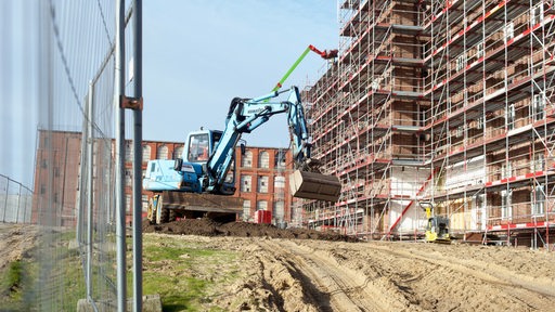 Bagger machen sich an großem Gebäude mit Gerüst zu schaffen