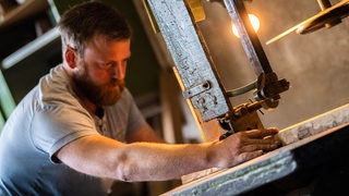 Der Fassbauer Christoph Krogemann sägt in seiner Fassfabrik an einem Holzbrett. 