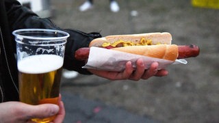 Eine Person hält einen Bierbecher und eine Bratwurst in den Händen