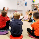 Schüler einer Grundschulklasse sitzen während des Unterrichts in einem Kreis auf dem Boden des Klassenzimmers zusammen und melden sich.