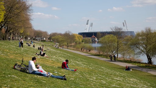 Menschen geniessen die Sonne am Osterdeich an der Weser, im Hintergrund sieht man das Weser-Stadion.