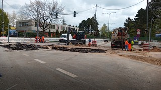 Baurarbeiter arbeiten in einer Baustelle an einer aufgerissenen Straße.