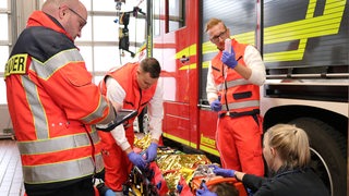 Mehrere Personen in Sanitäter-Kleidung stehen vor einem Feuerwehrauto um eine Person auf einer Trage herum.