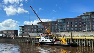 Ein Schiff liegt vor einem Kran am Wasser.