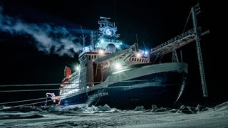 Die Polarstern liegt in der Dunkelheit im Eis und stößt Rauch aus.