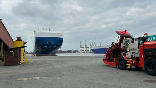 Ein blau-weißes Schiff liegt an einem Kai in einem Hafengebiet.