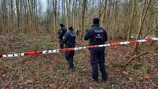 Mehrere Polizisten stehen hinter einer Absperrung im Wald.