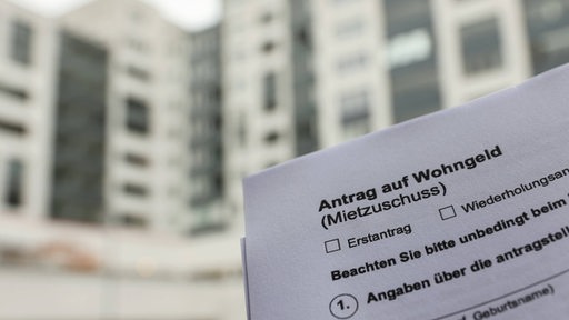 Der Ausdruck eines Antrags auf Wohngeld ist vor einem Hochhaus zu sehen. 