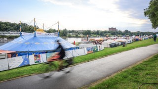 Ein Radfahrer fährt am Eröffnungsabend der Breminale am Osterdeich an der Weser in Bremen an Zelten und Buden vorbei. 