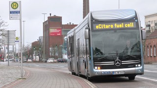 Ein Bus hält auf einer Straße neben einem Haltestellenschild.