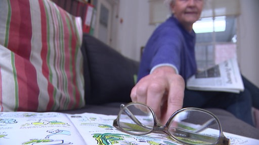 eine Frau greift nach ihrer Brille, die auf einem Buch liegt