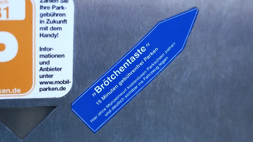 Auf einem Parkscheinautomat ist ein blauer Pfeil mit der Aufschrift "Brötchentaste" zu sehen.