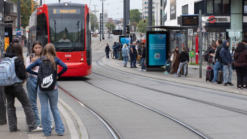 Fahrgäste stehen an der Haltestelle Domsheide in Bremen während eine Bahn einfährt.