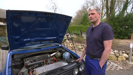 Markus Heuer steht neben einem Auto mit einer geöffneten Motorhaube.